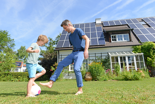 A photo of a man and a boy playing soccer in front of a house with a solar panel installation