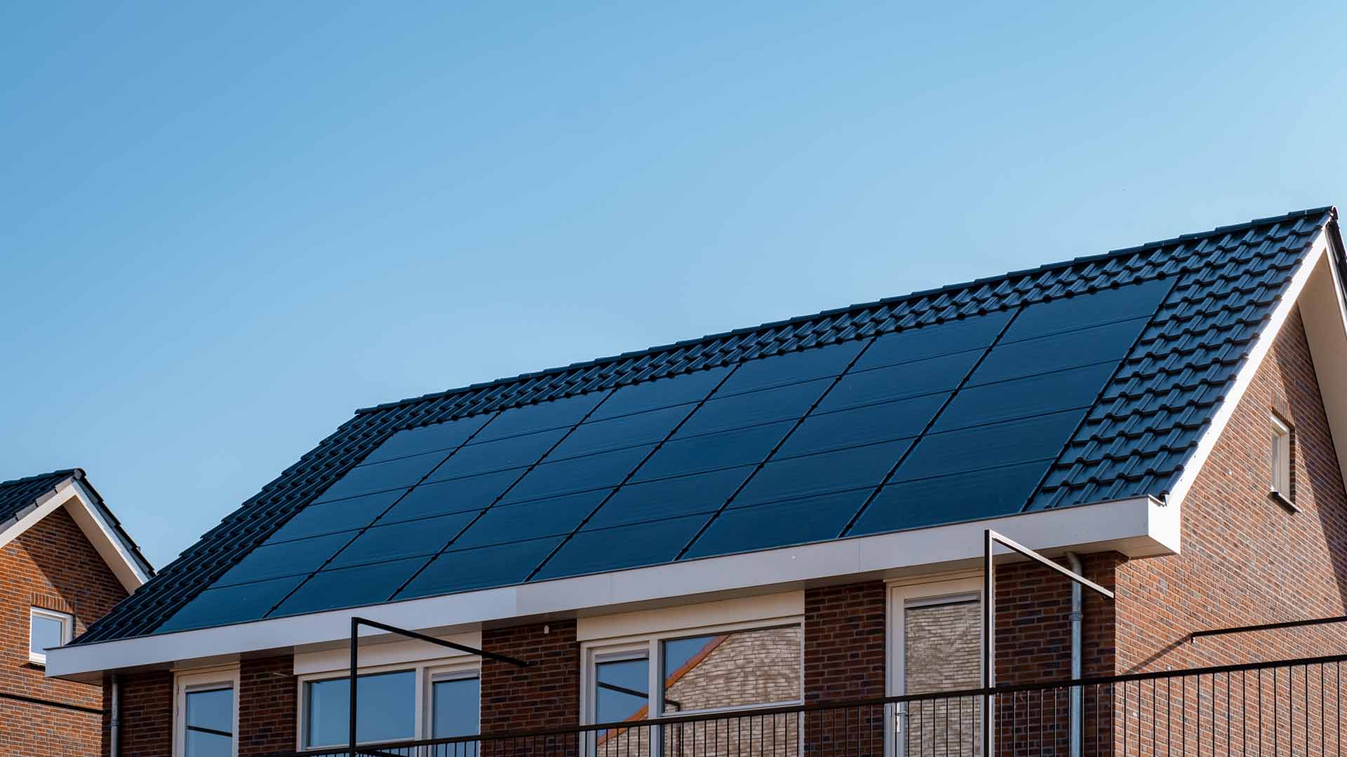 Newly build houses with solar panels attached on the roof against a sunny sky Close up of a new building with black solar panels. Zonnepanelen, Zonne energie, Translation: Solar panel, , Sun Energy.